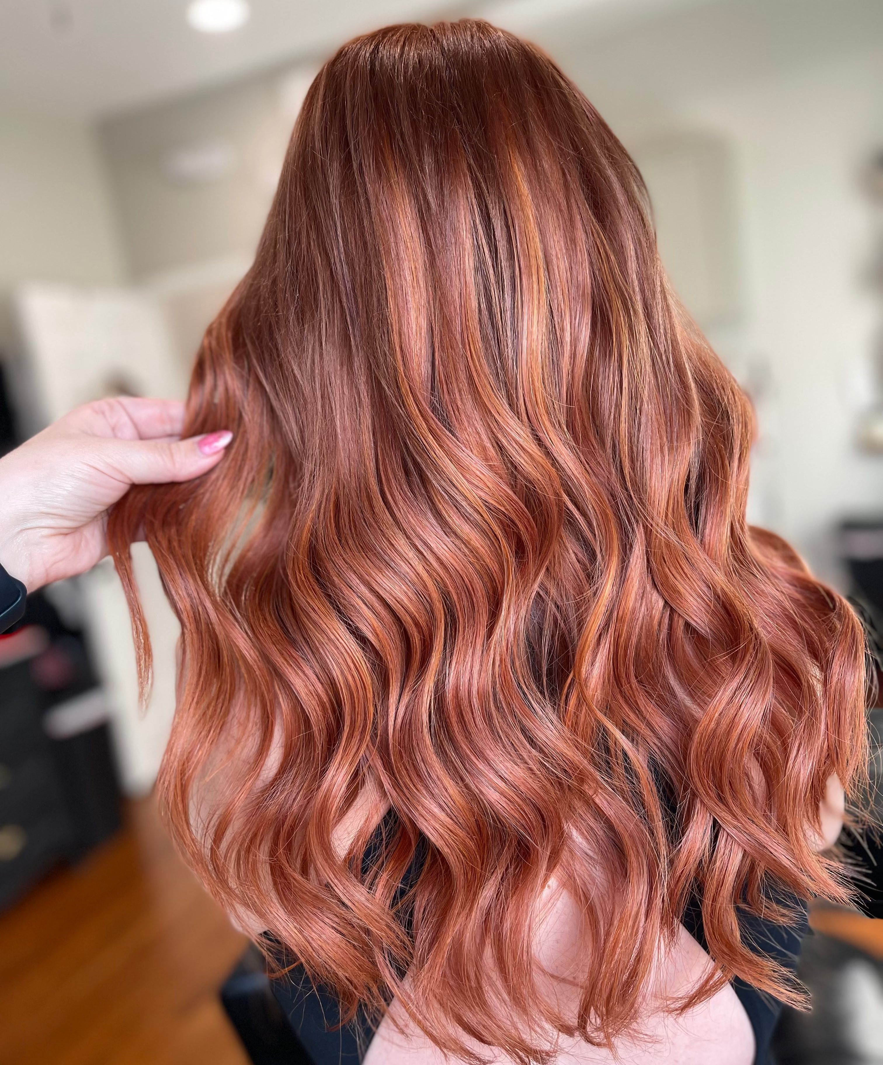long hair with extensions. Woman with wavy, rose gold hair in a salon setting